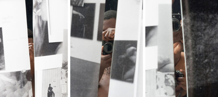 Man points a camera at viewer, surrounded by papers.