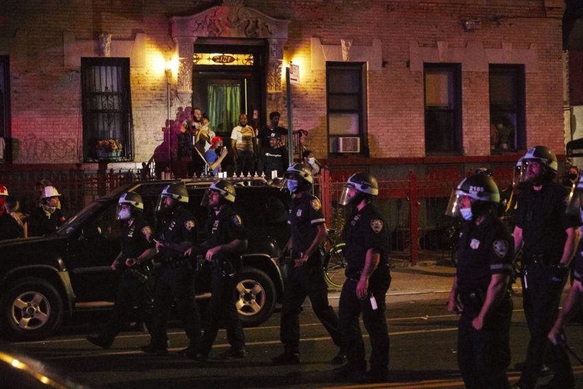 Civilians photograph a line of police officers marching down the street