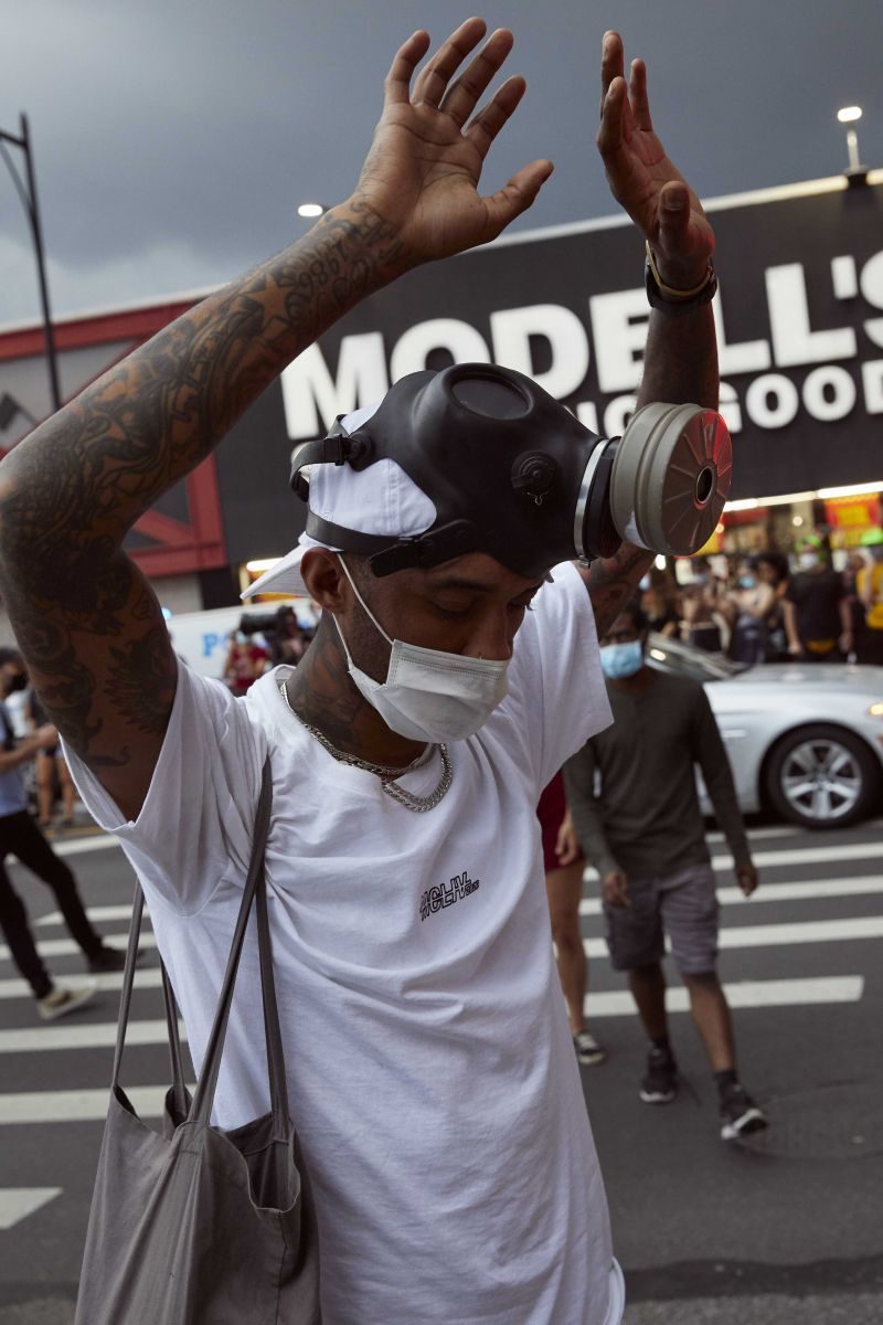 A young Black man holds his hands up above his head