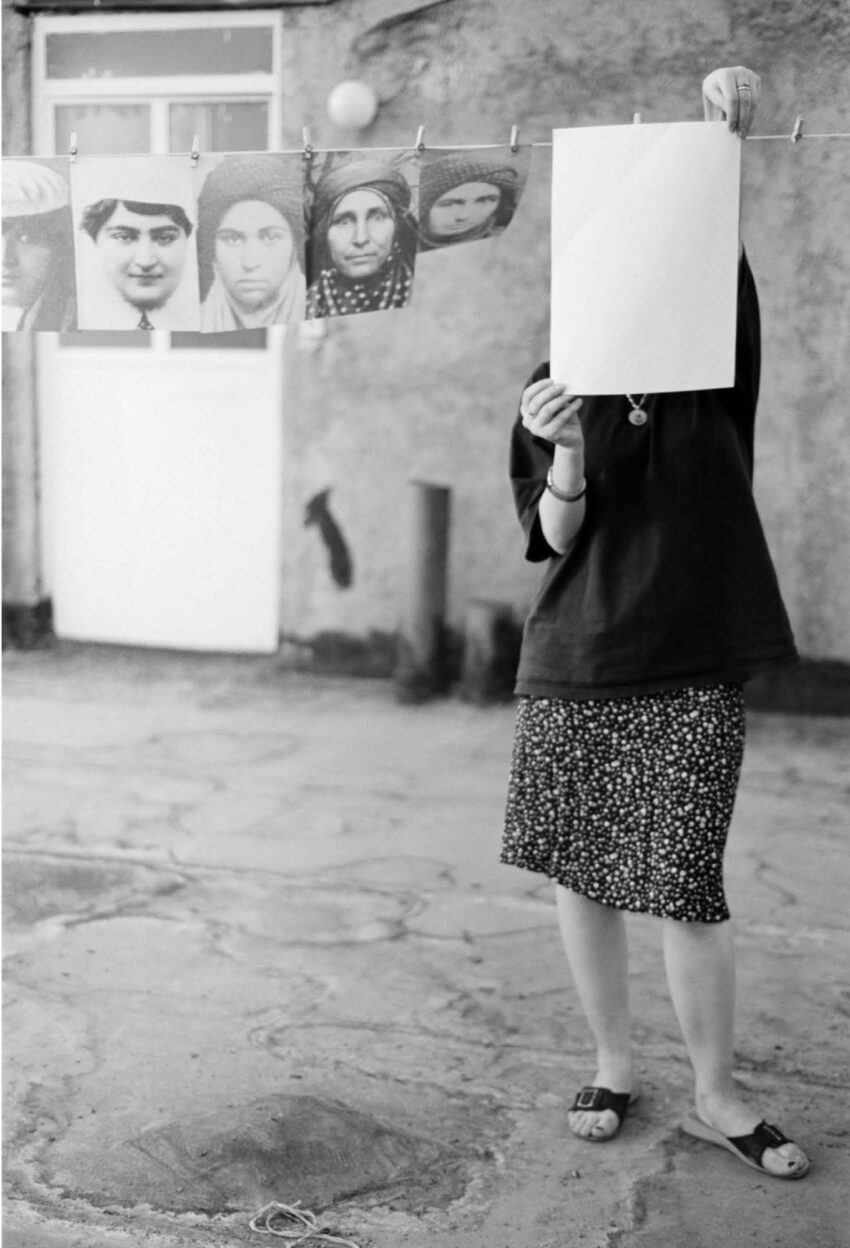 A woman holds up a paper to clip it to a drying line with other images