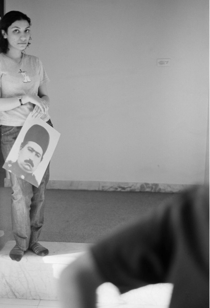 A woman holds a photograph of a man in a hat