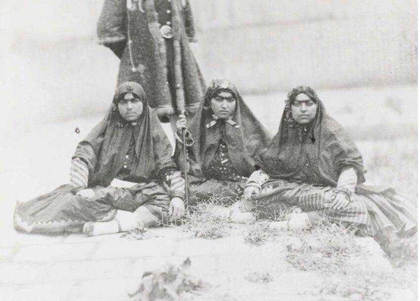 Three women sit in traditional garb, a fourth person standing behind them