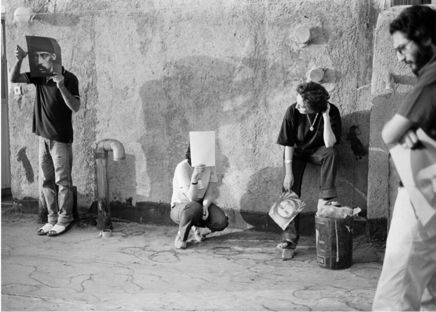 A group of people stand in various postures before a wall