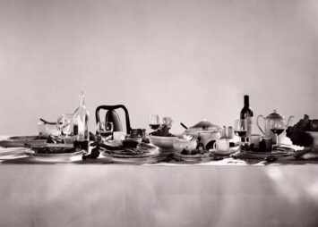 Grayscale image of a tablescape set with glasses of wine and an overflowing bowl of fruit