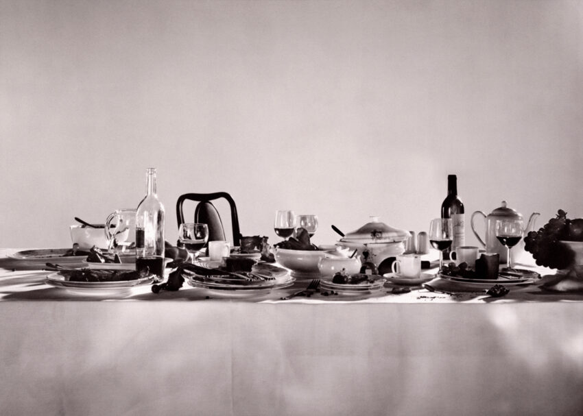 Grayscale image of a tablescape set with glasses of wine and an overflowing bowl of fruit