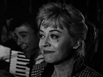 Black and white still showing Giulietta Masina smiling with a black tear at the corner of her eye