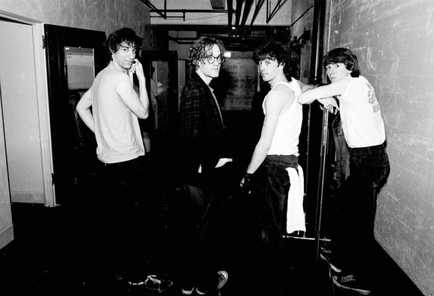 Black-and-white photo of R.E.M.’s band members standing in a backstage hallway