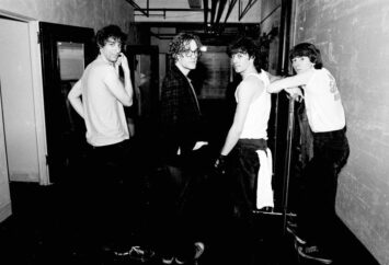 Black-and-white photo of R.E.M.’s band members standing in a backstage hallway
