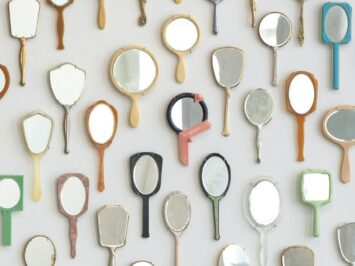 Installation of found hand mirrors arranged in an oval on a wall.